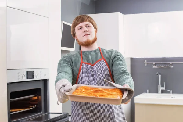 Joven con barba roja haciendo pastel en la cocina moderna blanca — Foto de Stock