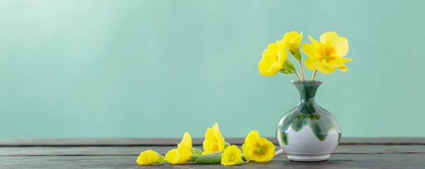 Yellow primroses in vase on wooden table — Stock Photo, Image