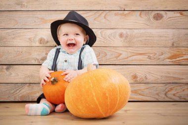 Siyah şapkalı bebek ve tahta arka planda balkabakları.