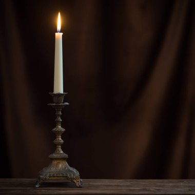 Arkadaki eski ahşap masada yanan mumla kadife perdeli antik şamdan.