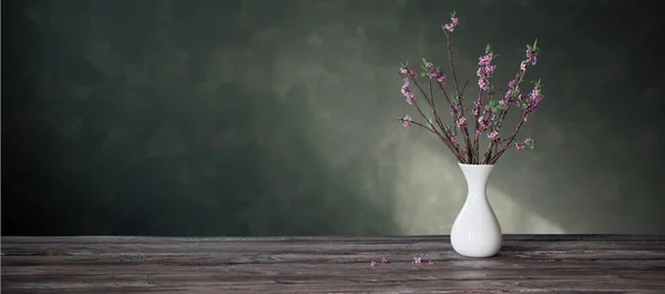 背景绿墙上的旧木桌上花瓶里的达芙妮花 — 图库照片
