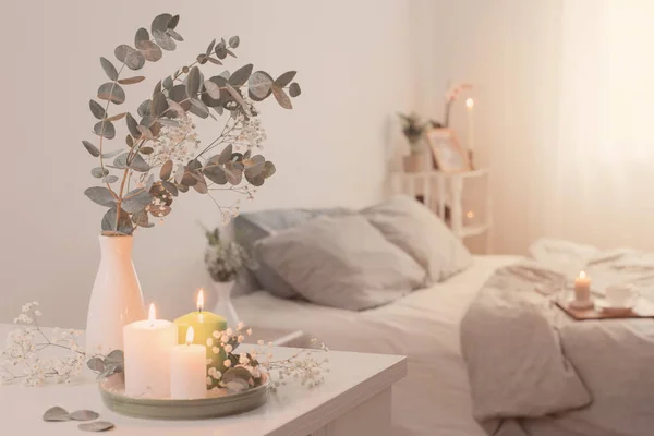 burning candles and eucalyptus in  vase in white bedroom