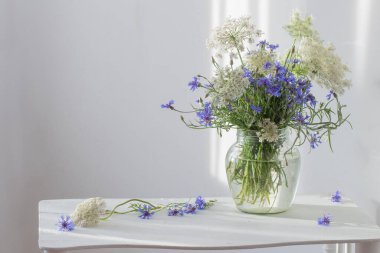 Beyaz ahşap rafta, kavanozda bir buket çiçek.