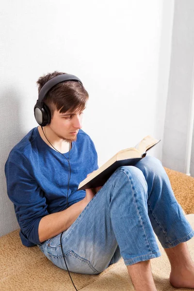 Hombre Joven Con Auriculares Leer Libro Sobre Sofá Hogar —  Fotos de Stock