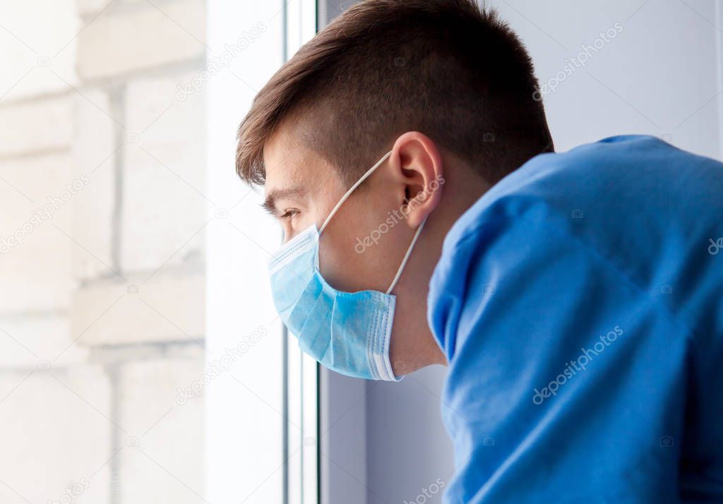 Young Man in a Flu Mask by the Window in the Room