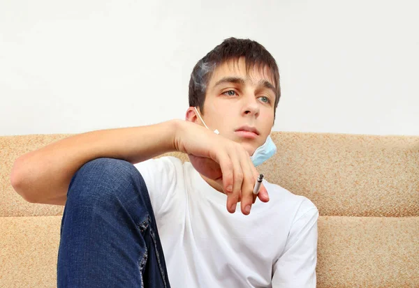 Junger Mann Mit Grippemaske Raucht Zigarette Auf Dem Sofa — Stockfoto