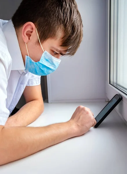 Young Man in Flu Mask by the Window with a Mobile Phone