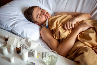 Hasta genç adam evdeki yatakta termometreyle uyuyor.