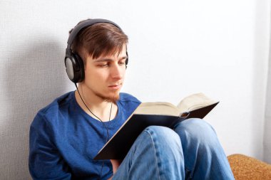 Kulaklıklı genç adam evde bir kitap okuyor.