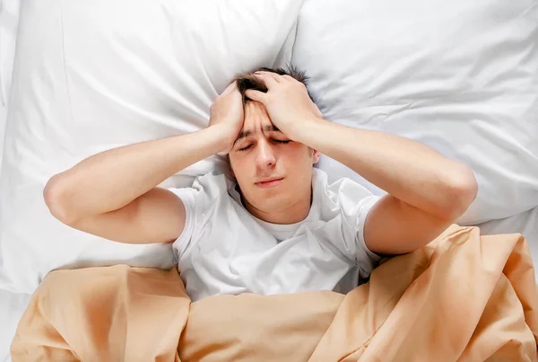 若い男は家のベッドで頭痛を感じる — ストック写真