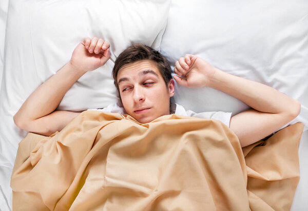 Tired and Sleepy Young Man in the Bed at the Home