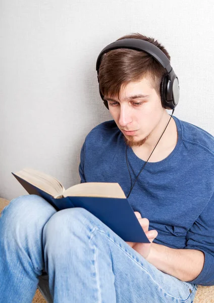 Kulaklıklı Genç Adam Evdeki Kanepe Üzerine Bir Kitap Okuyor — Stok fotoğraf
