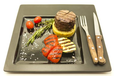 Mignon biftek ile kızarmış patates ve bıçak ile güzel bir siyah plaka üzerinde ızgara sebzeler ve beyaz bir arka plan üzerinde çatalı.