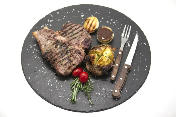 Šťavnatý hovězí steak středně propečený na kámen pečené brambory a barbecue omáčkou a velké mořské soli s vidličkou a nožem. — Stock fotografie