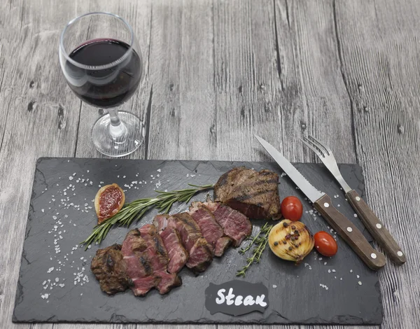 Grilled striploin steak on a stone plate with a glass of red wine with a fork and knife.