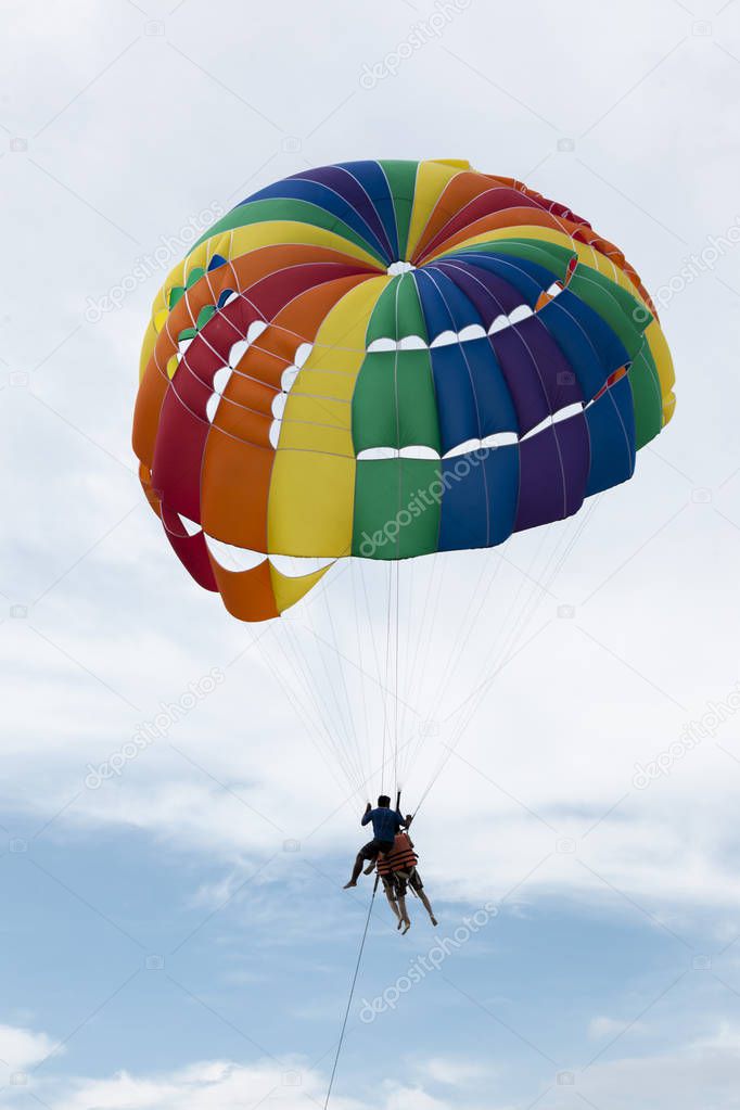 Beautiful color large parachute in the blue sky tropical beach. Two Chinese tourists flying on a parachute over the sea on a beach in Phuket Thailand.