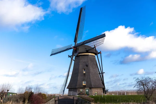 Традиционная голландская ветряная мельница возле канала. Нидерланды. Старая ветряная мельница стоит на берегу канала, и водяные насосы. Белые облака на голубом небе, ветер дует . — стоковое фото