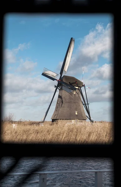 Moinho de vento holandês tradicional perto do canal. Países Baixos. Velho moinho de vento fica nas margens do canal, e bombas de água. Nuvens brancas num céu azul, o vento sopra . — Fotografia de Stock