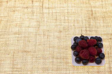 Taze yaban mersini, ahududu beyaz bir plaka üzerinde bir plaka üzerinde bir keten arka plan closeup closeup üzerinde. Şekerleme için arka plan, café taze çilek pasta için.