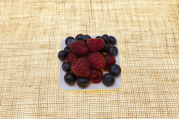 Fresh blueberries, raspberries on a white plate, closeup on a plate on a linen background closeup. Background for confectionery, cafe fresh berries for pastry. — Stock Photo, Image