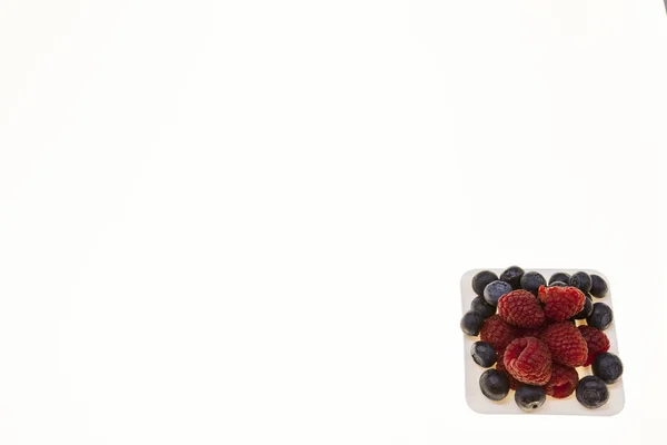 Frische Blaubeeren, Himbeeren auf einem weißen Teller, Nahaufnahme auf weißem Hintergrund. Hintergrund für Süßwaren, Café frische Beeren für Gebäck. — Stockfoto