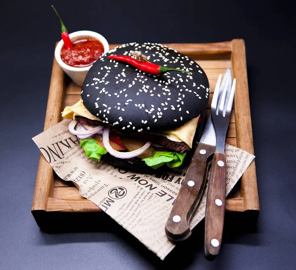 Un burger noir juteux. Burger au bœuf de marbre, fourchette au couteau et sauce chili sur le journal — Photo