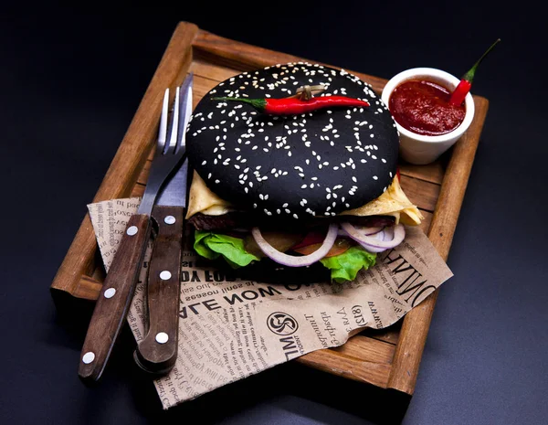 Einen saftigen schwarzen Burger. Burger mit Marmor-Rindfleisch, Gabel mit Messer und Chilisoße auf der Zeitung — Stockfoto