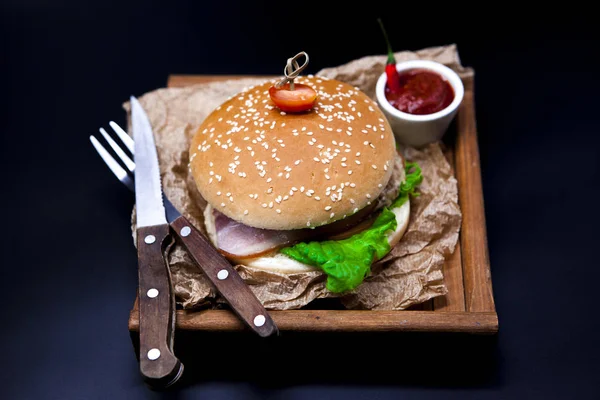 Un hamburger succoso. Hamburger con carne di marmo, forchetta con coltello e salsa di peperoncino sul giornale — Foto Stock