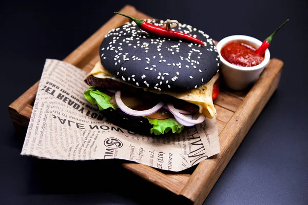 Um hambúrguer preto suculento. Hambúrguer com carne de mármore, garfo com faca e molho de pimenta no jornal — Fotografia de Stock