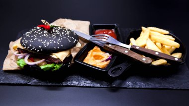 Lezzetli set: hamburger, patates kızartması, köri sos, biber sosu, çatal ve bıçak.