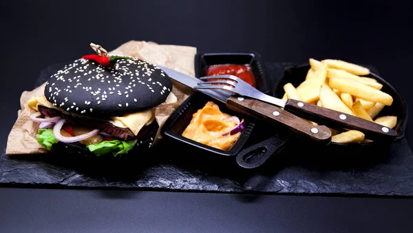 Delicioso conjunto: hambúrguer, batatas fritas, molho de caril, molho de pimenta, garfo e faca . — Fotografia de Stock