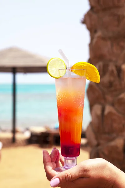 Copo de vidro com um cocktail na mão de uma menina na praia . — Fotografia de Stock