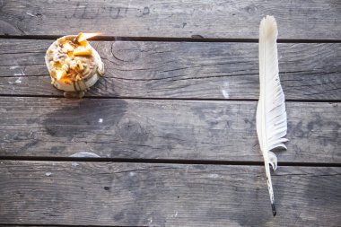 Yanan bir mumla yazmak için tüy. Tüy yanan bir mumla eski bir ahşap masanın üzerinde yatıyor. Peçeteler, duvar kağıtları, kitaplar, defterler, kâğıtlar için harika bir arka plan. Retro biçimi, eski zaman