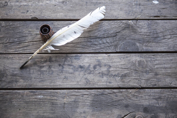 Feather for writing and inkwell .Quill for writing. The feather lies on an old wooden table with inkwell . Beautiful background for napkins, wallpapers, books, notebooks, paper. Retro style, olden time