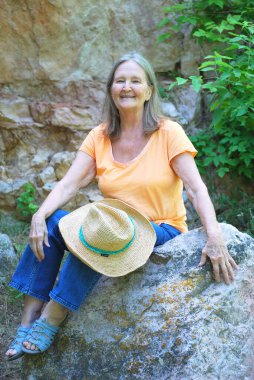 Dışarıda kayaların üzerinde oturan olgun yaşlı kadın ifadeleri..