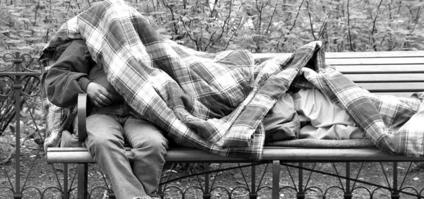 屋外の公園のベンチで毛布の下で寝ているホームレスの男性 — ストック写真