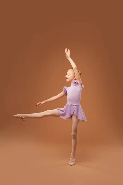 Усміхнена дівчина в фіолетовій сукні показує елементи балету — стокове фото