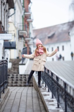 Kışın giyinmiş güzel bir kız eski bir sokakta yürüyor.