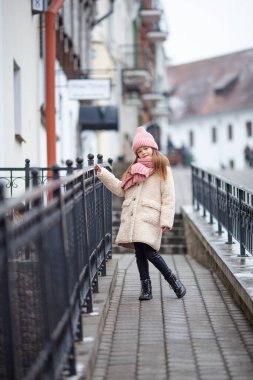 Kışın giyinmiş güzel bir kız eski bir sokakta yürüyor.