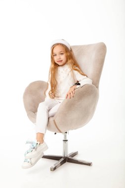 Uzun saçlı, beyaz elbiseli bir kız, sandalyeye oturuyor.