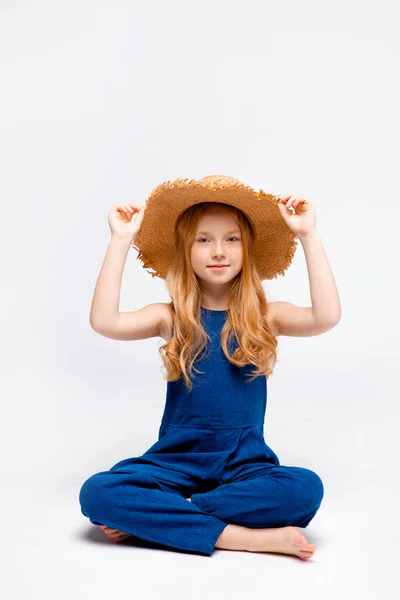 Rothaarige Mädchen Blauen Overalls Und Strohhut Mit Überkreuzten Beinen — Stockfoto