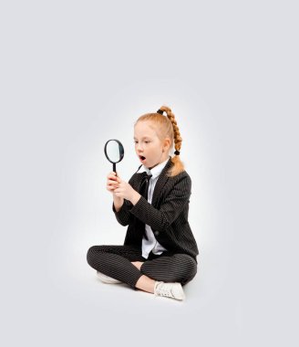 girl in a business black suit sits cross-legged and looks in surprise through a magnifying glass. clipart