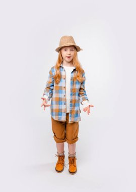 Uzun saçlı, gezgin elbiseli duygusal kız açık gri bir arka planda duruyor.