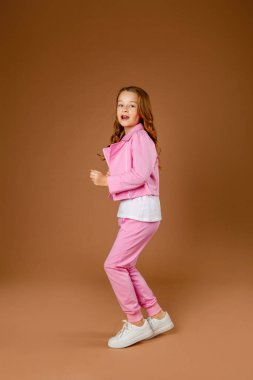 Pembe eşofmanlı kız jimnastik yapıyor ve bej arka planda egzersiz yapıyor.