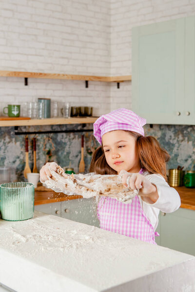 girl in the kitchen kneads dough and sprinkled flour
