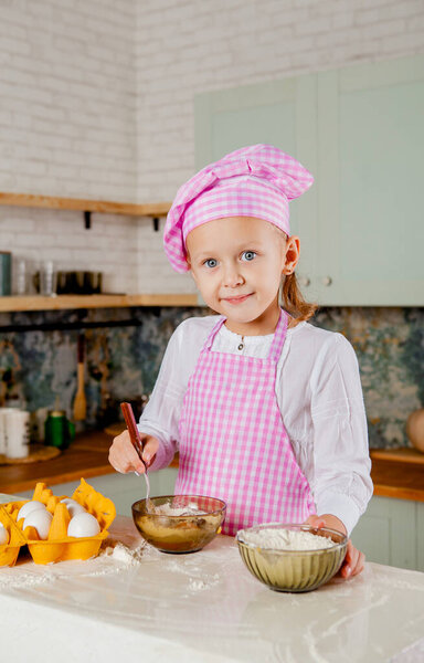 Girl in a chef's hat and apron kneads dough