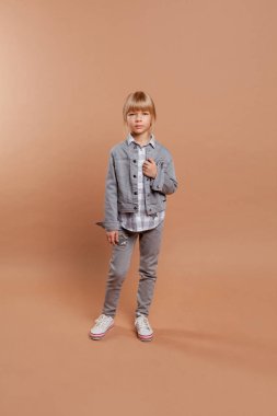 Günlük giysiler içinde güzel bir kız (kot, ceket, spor ayakkabısı) bej bir arka planda