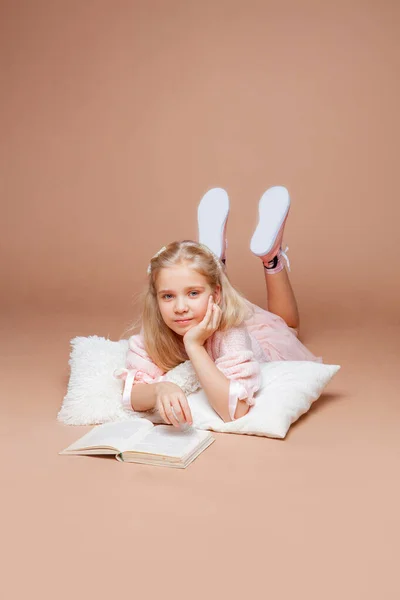 Blondes Mädchen Liegt Auf Rosa Hintergrund Und Liest Ein Buch — Stockfoto