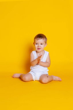 Tişört ve iç çamaşırlı çocuk turuncu-sarı arka planda oturuyor.