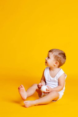 Tişörtlü ve külotlu bir çocuk ellerinde beyaz bir Noel topuyla turuncu-sarı arka planda